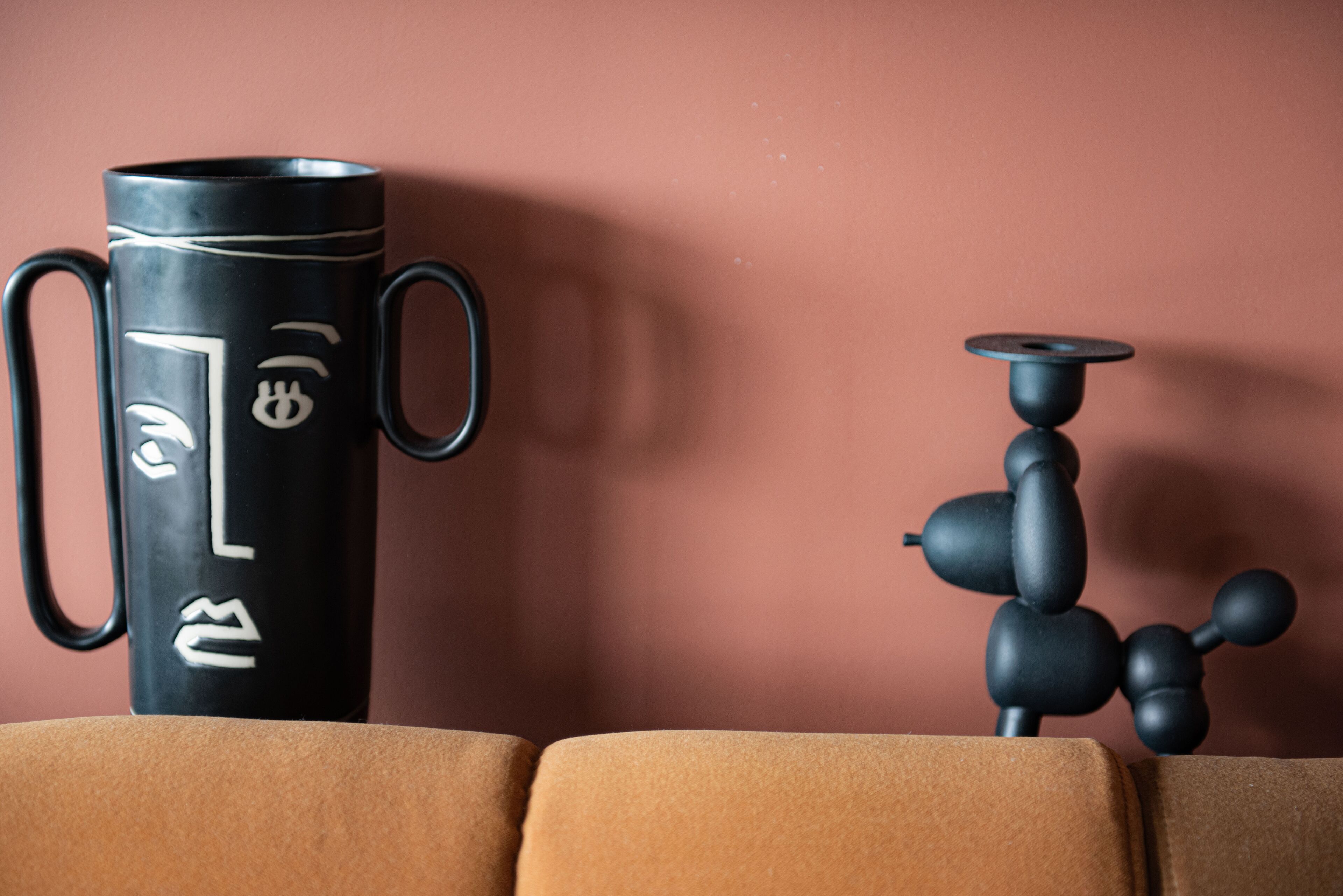 Een zwarte thermoskan en een zwarte shisha op een bruine bank voor een roze muur.