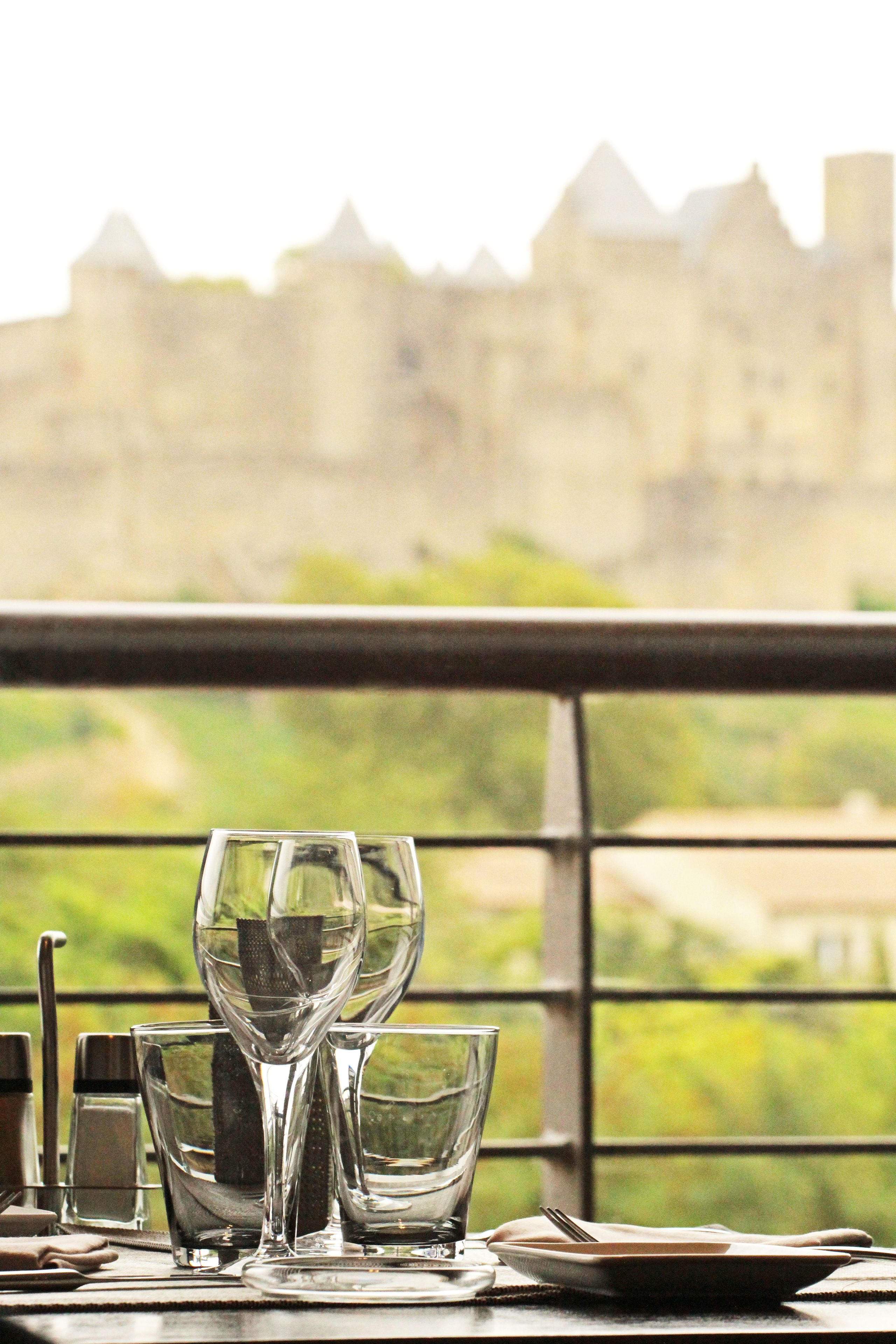 A table with glasses and cutlery, a plate, and a window with a view of a castle.