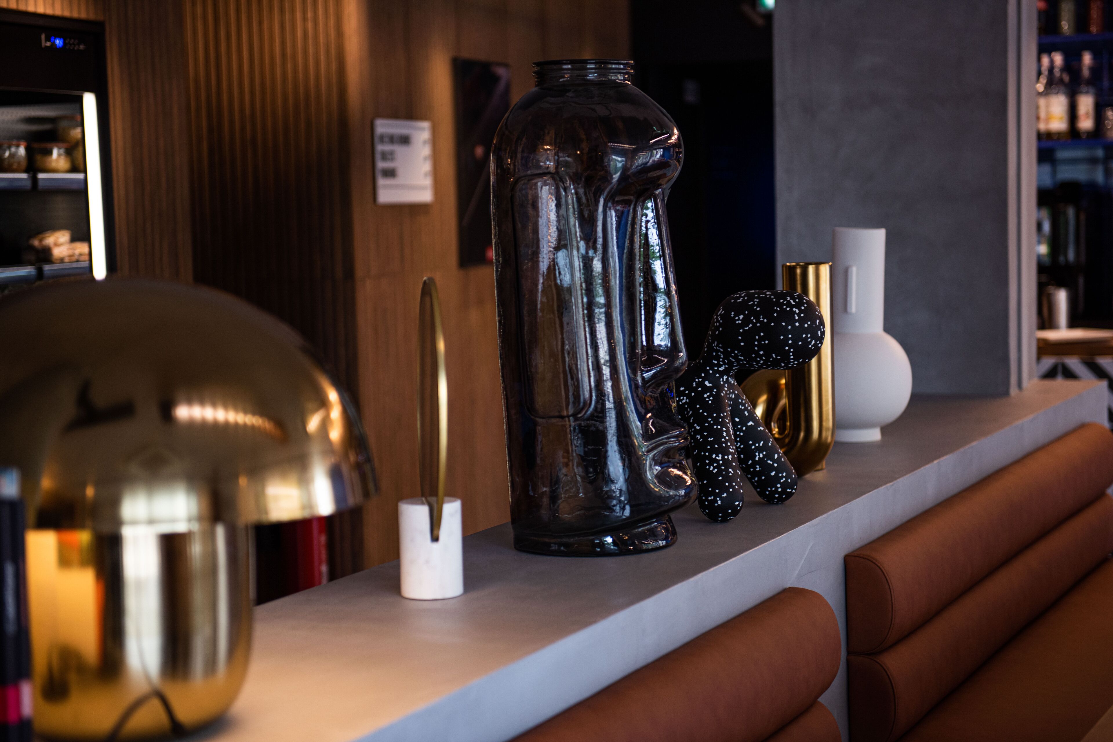 A bar area with a counter, a large glass pitcher, a gold-colored object, and a white vase.