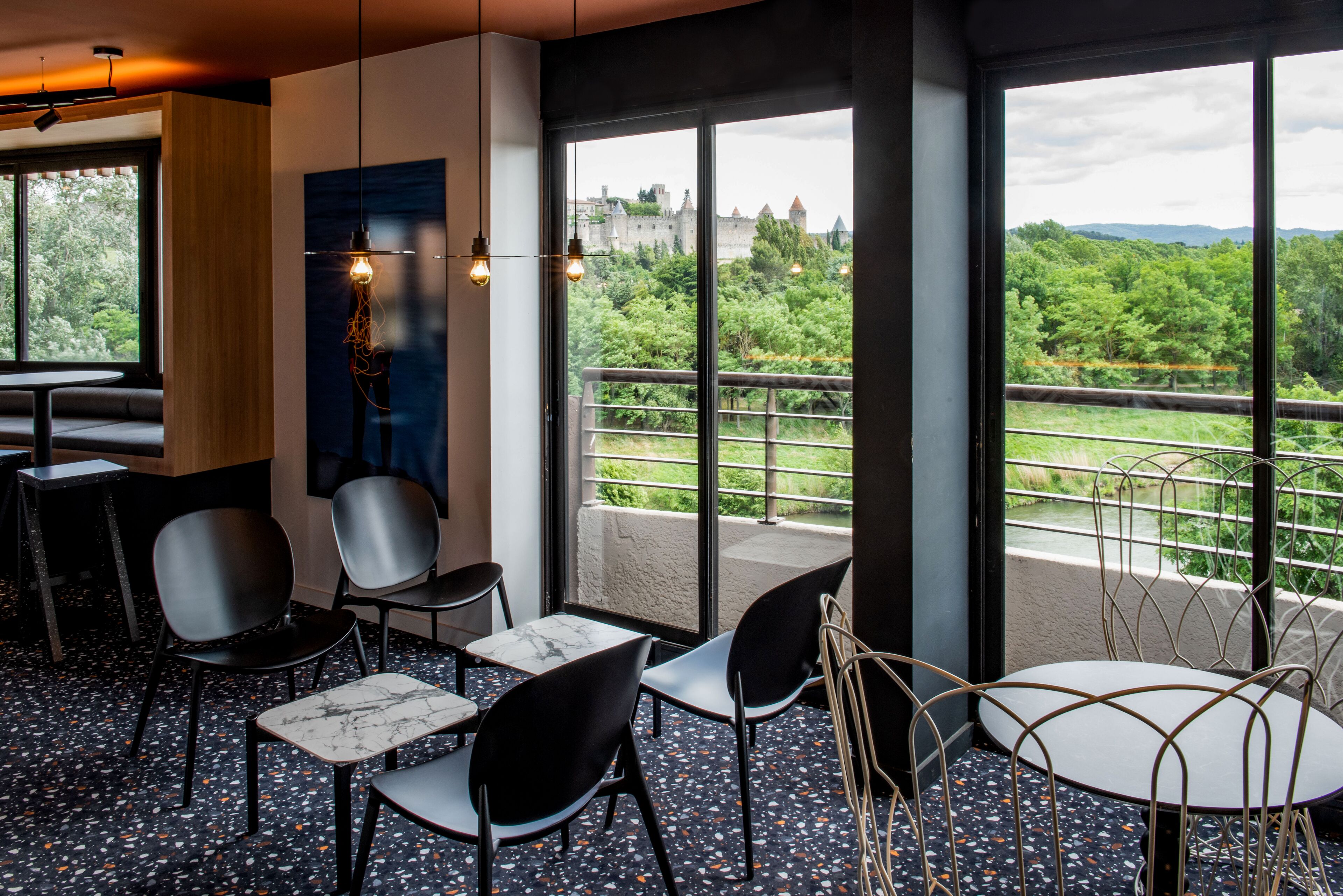 Un interior moderno con vistas a una terraza, con una variedad de arreglos de asientos y un amplio ventanal que da a la vegetación y un castillo lejano.