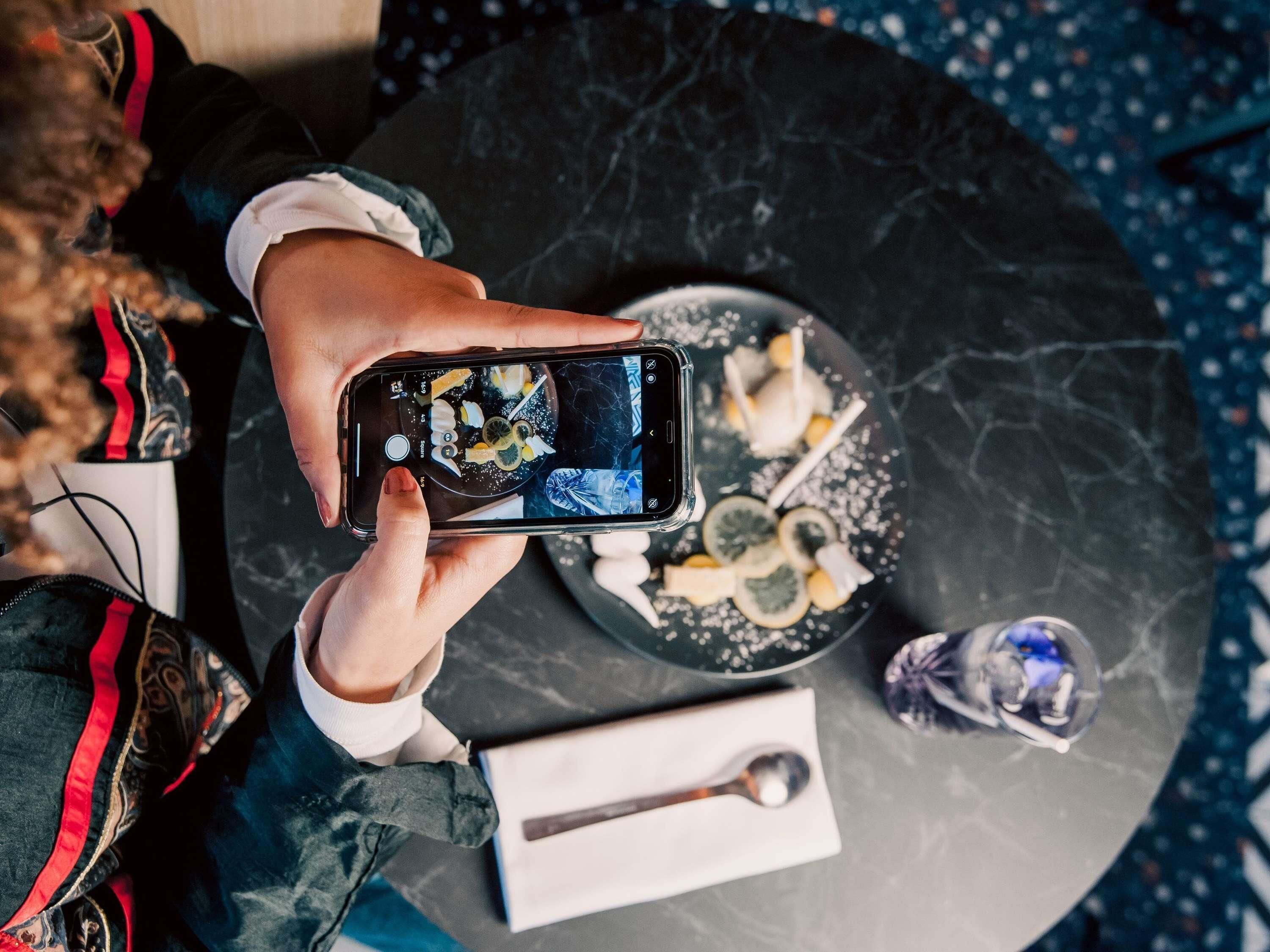 Una persona agafa un telèfon mòbil per fer una fotografia a un plat amb menjar i una cullera damunt una taula de marbre.