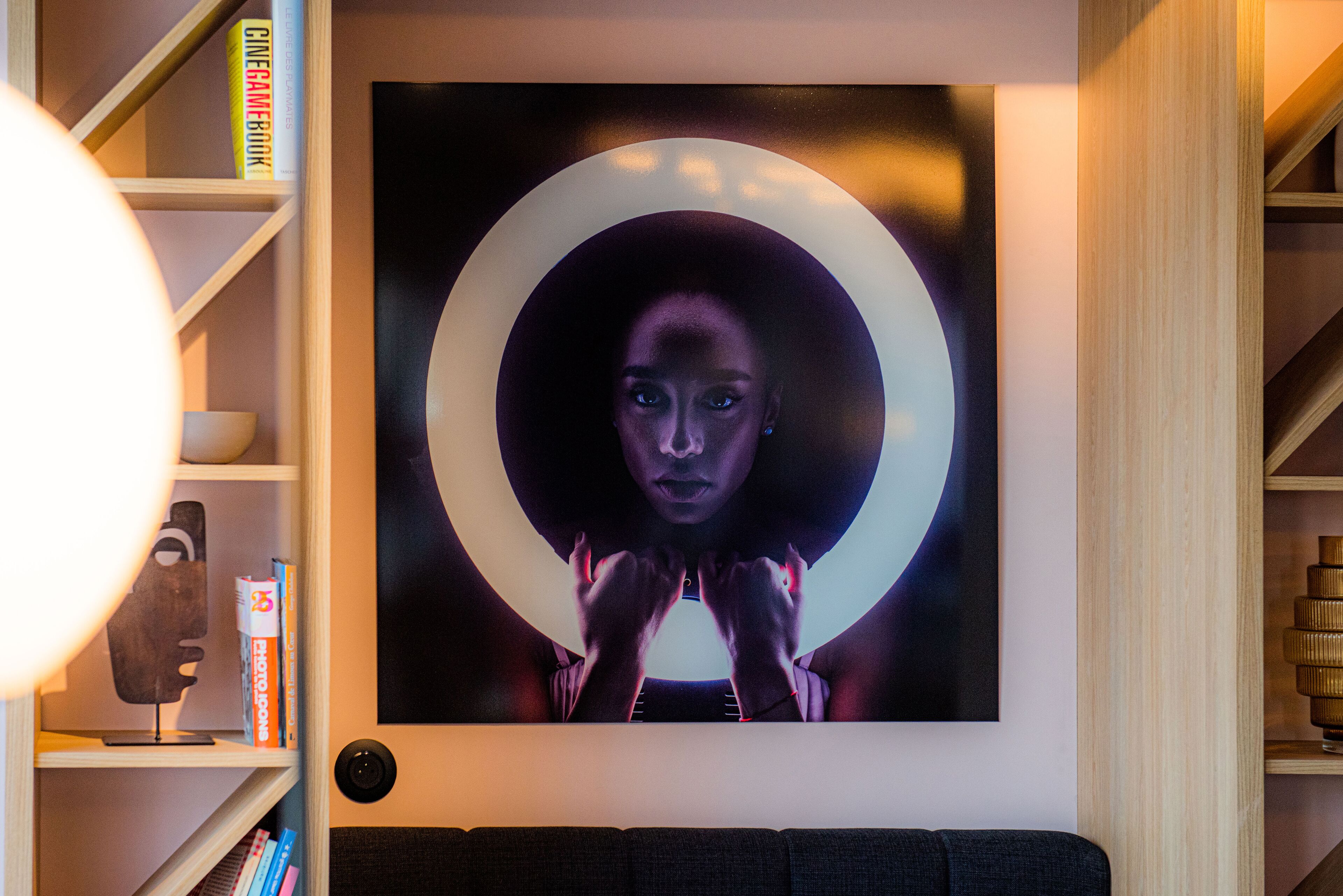 Un mur orné d’une œuvre d’art circulaire et une bibliothèque contenant des livres et une lampe.