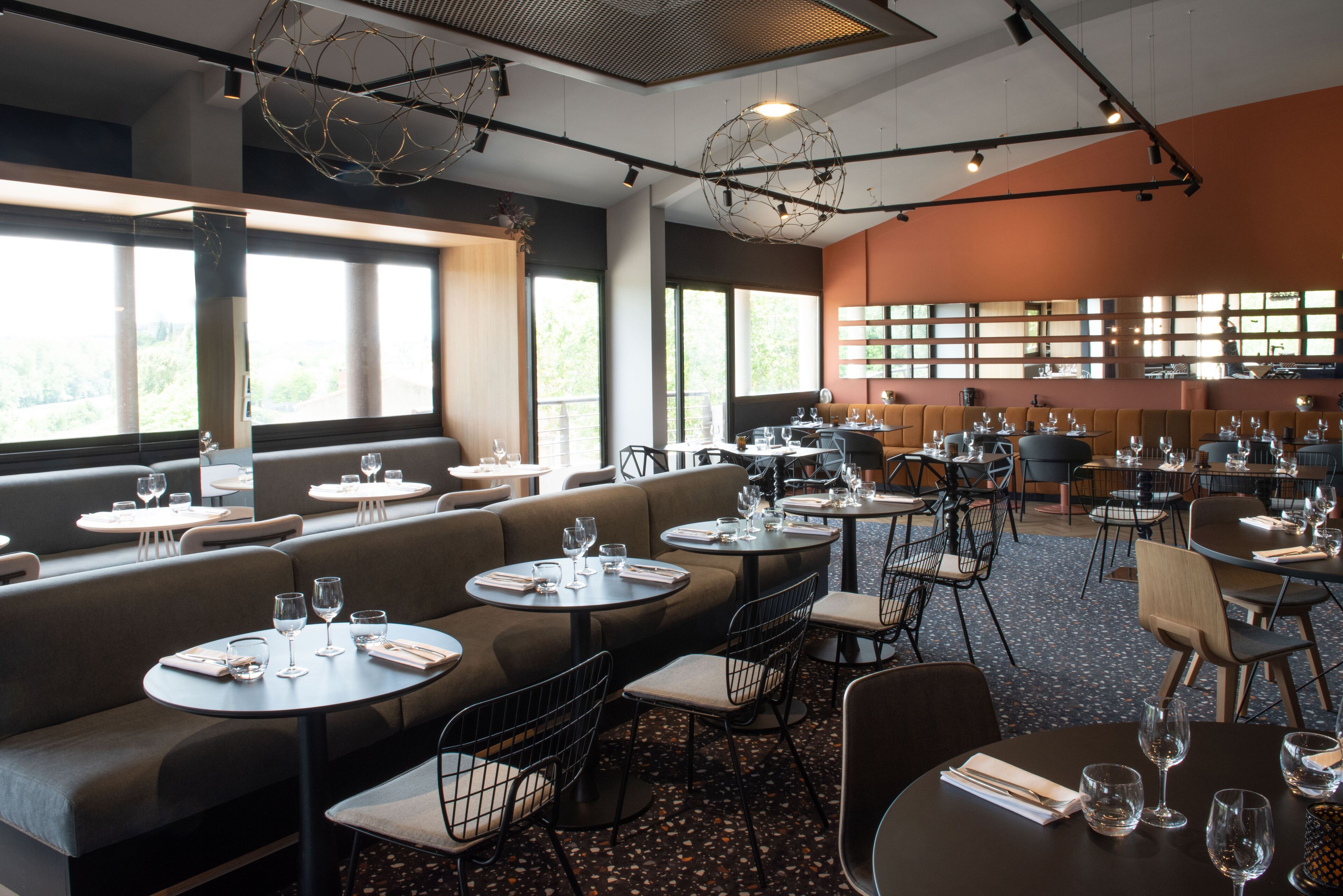 A restaurant with round tables, cushioned booths, and a large window overlooking greenery.