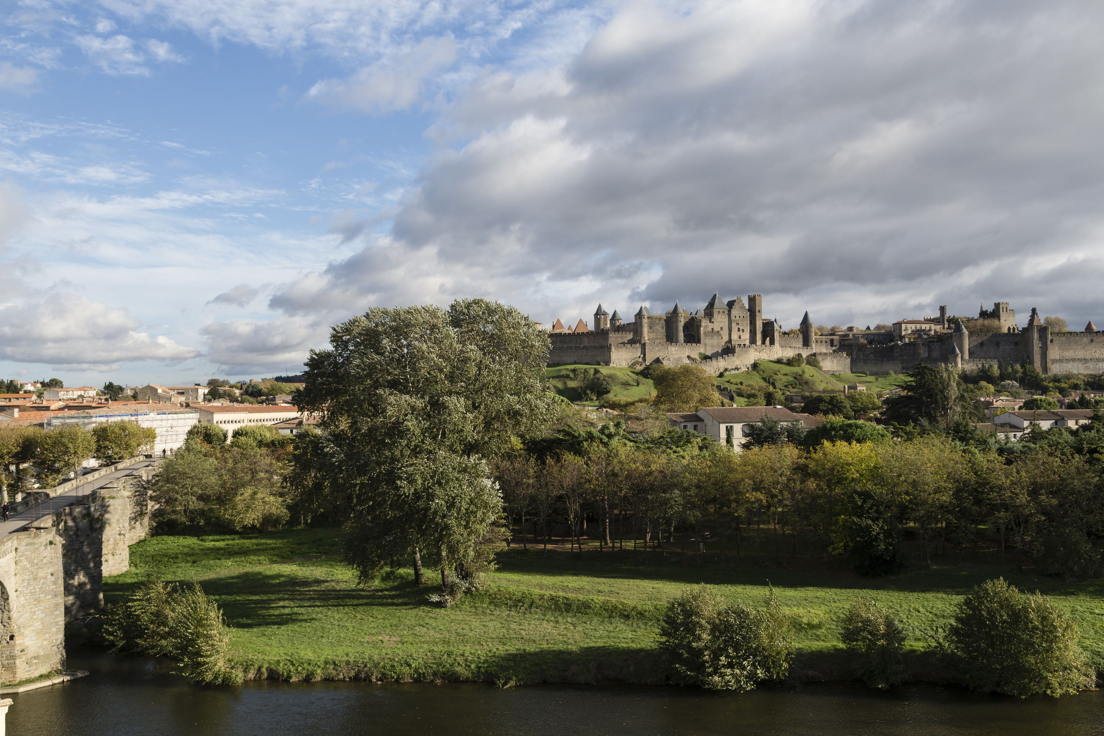 A historic castle with a river in the foreground, surrounded by greenery and a clear sky.