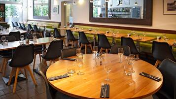 Ein Restaurant mit runden Tischen, schwarzen Stühlen und hängenden Pendelleuchten.