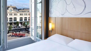 Habitación de hotel con un ventanal grande, una cama, una lámpara de pared y vistas a un edificio con cúpula.