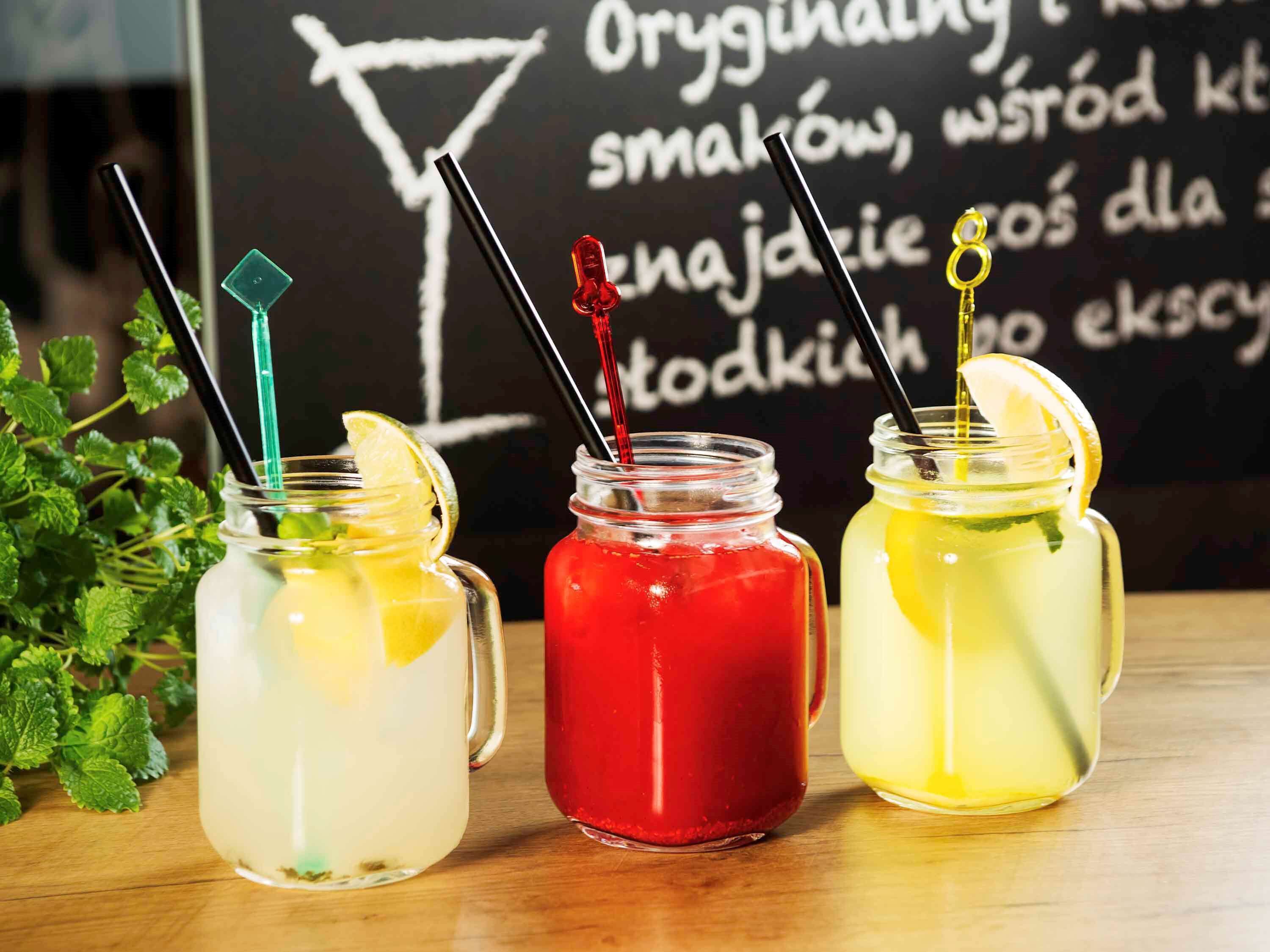 Three mason jars with straws and lemon slices on a wooden surface.
