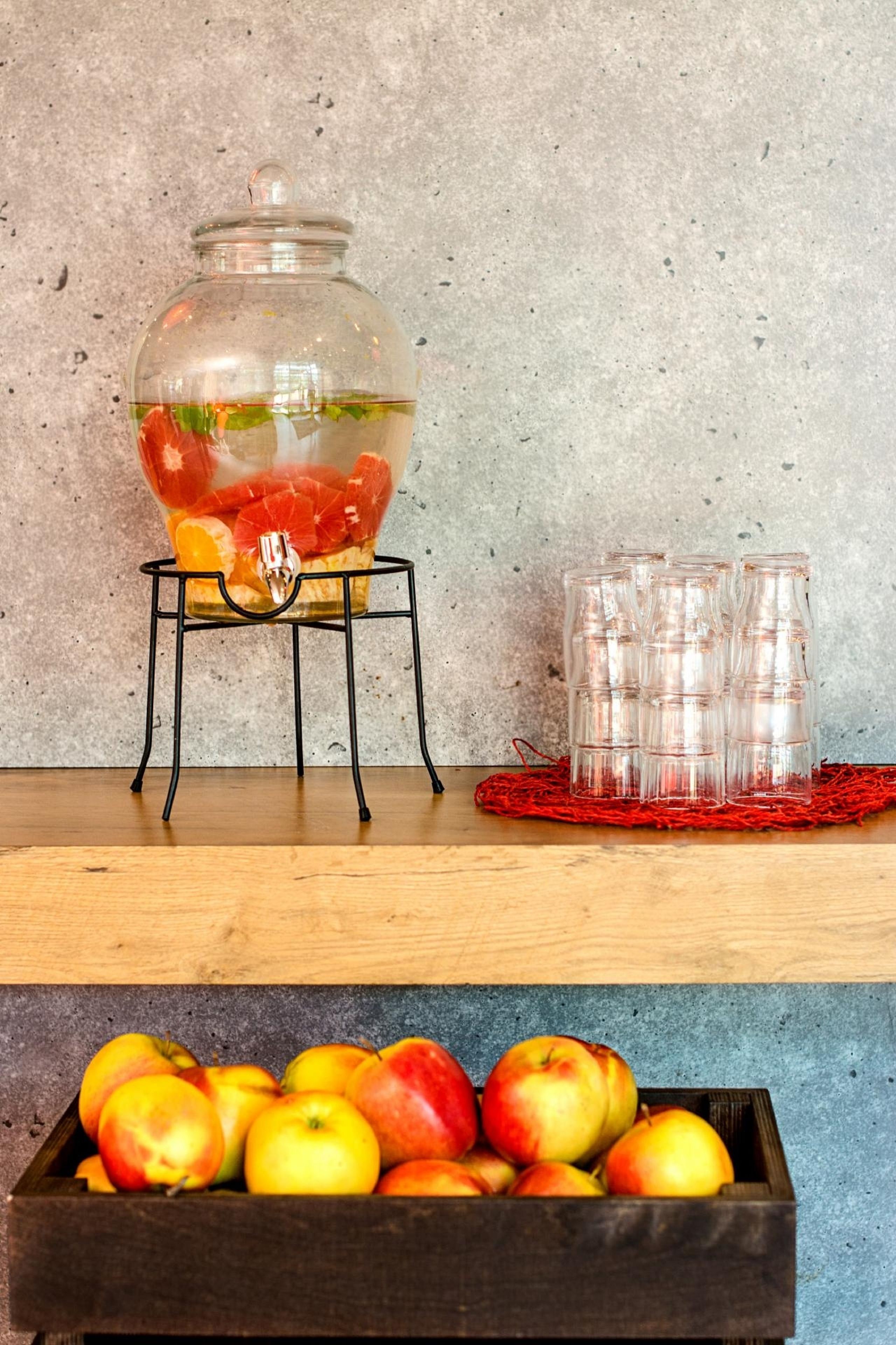 A fruit punch dispenser with oranges and a wooden crate of apples.