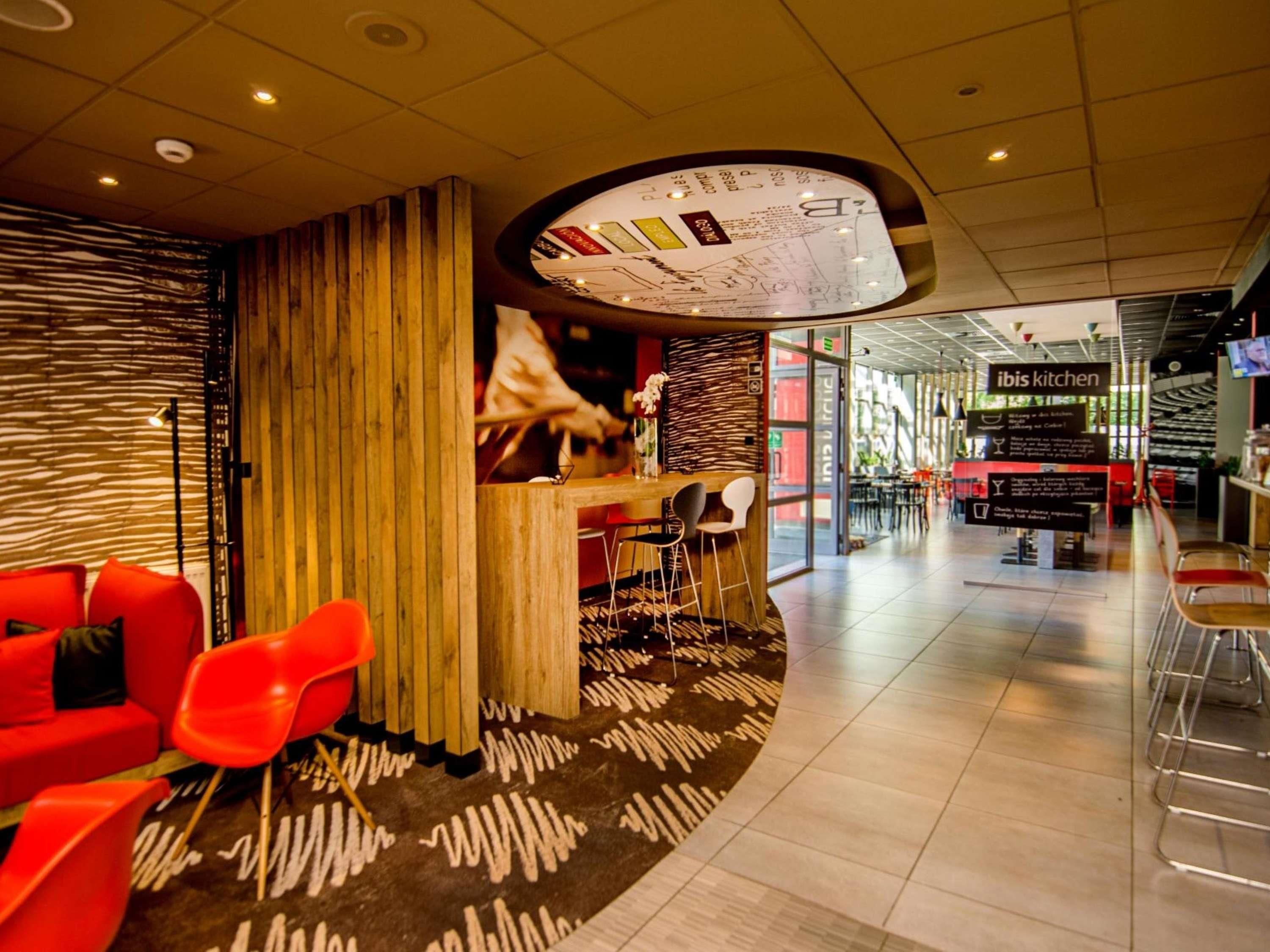 A modern interior with a wooden partition, red chairs, a bar area, and a sign for 'ibis kitchen'.
