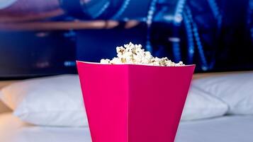 A pink popcorn container on a white surface with movie posters in the background.