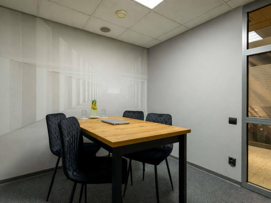 A conference room with a wooden table, four black chairs, a laptop, and a glass of water on the table.