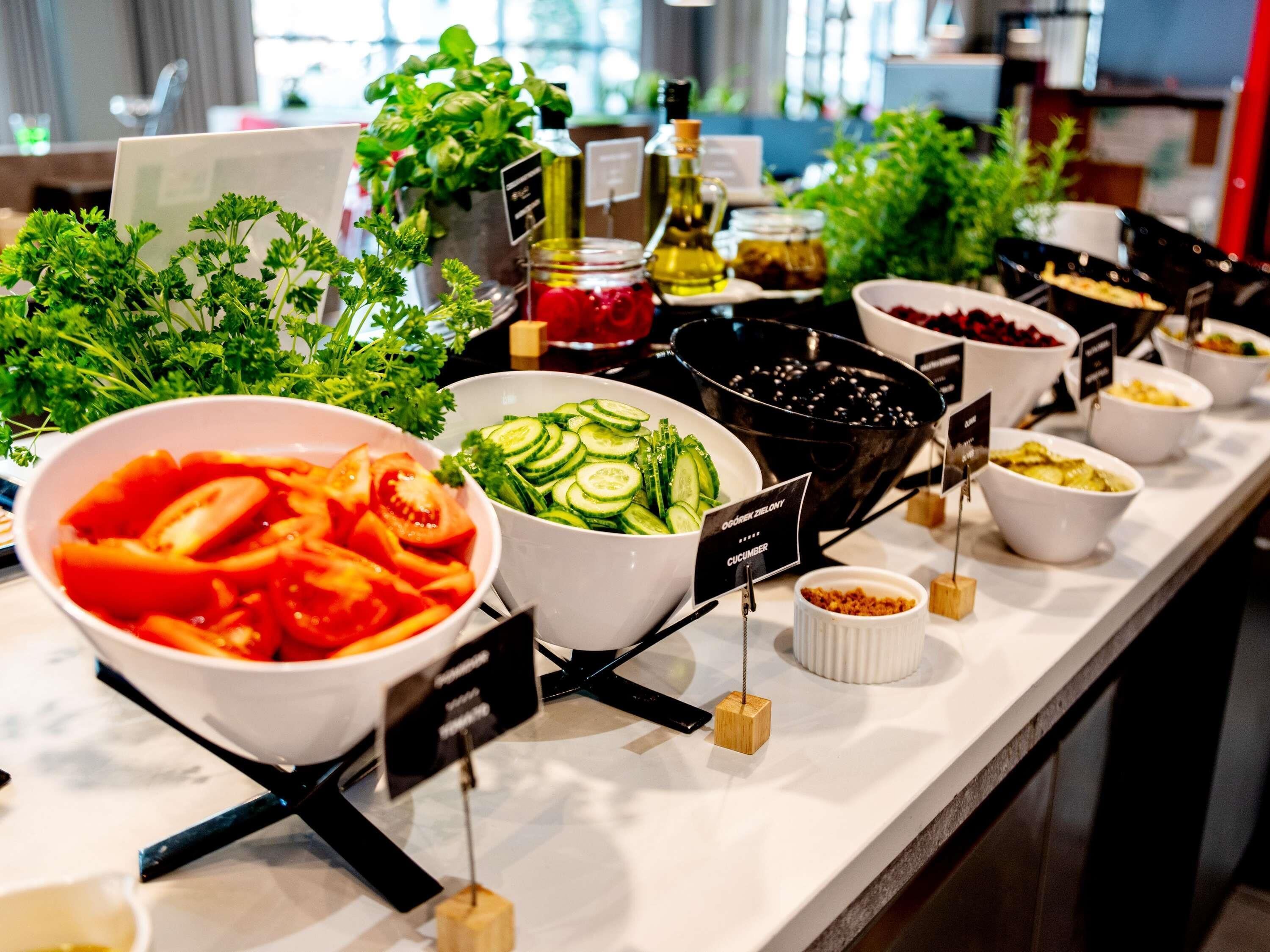 Ein Buffet mit verschiedenen Speisen, darunter eine Schüssel Tomatensuppe, Gurkensalat und eine schwarze Schüssel mit Oliven.