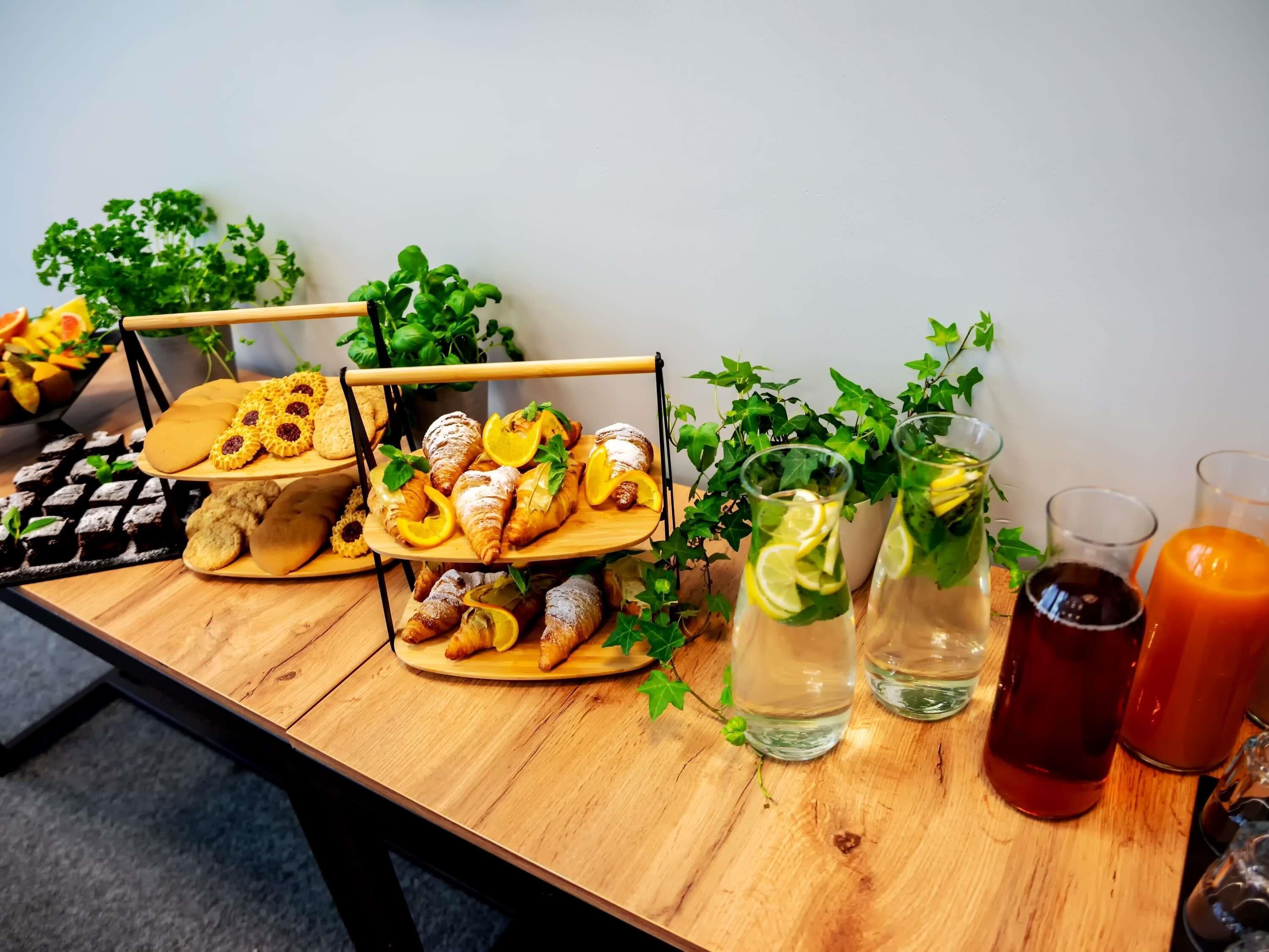 A wooden table with pastries, glasses of water and tea, and a waffle iron.