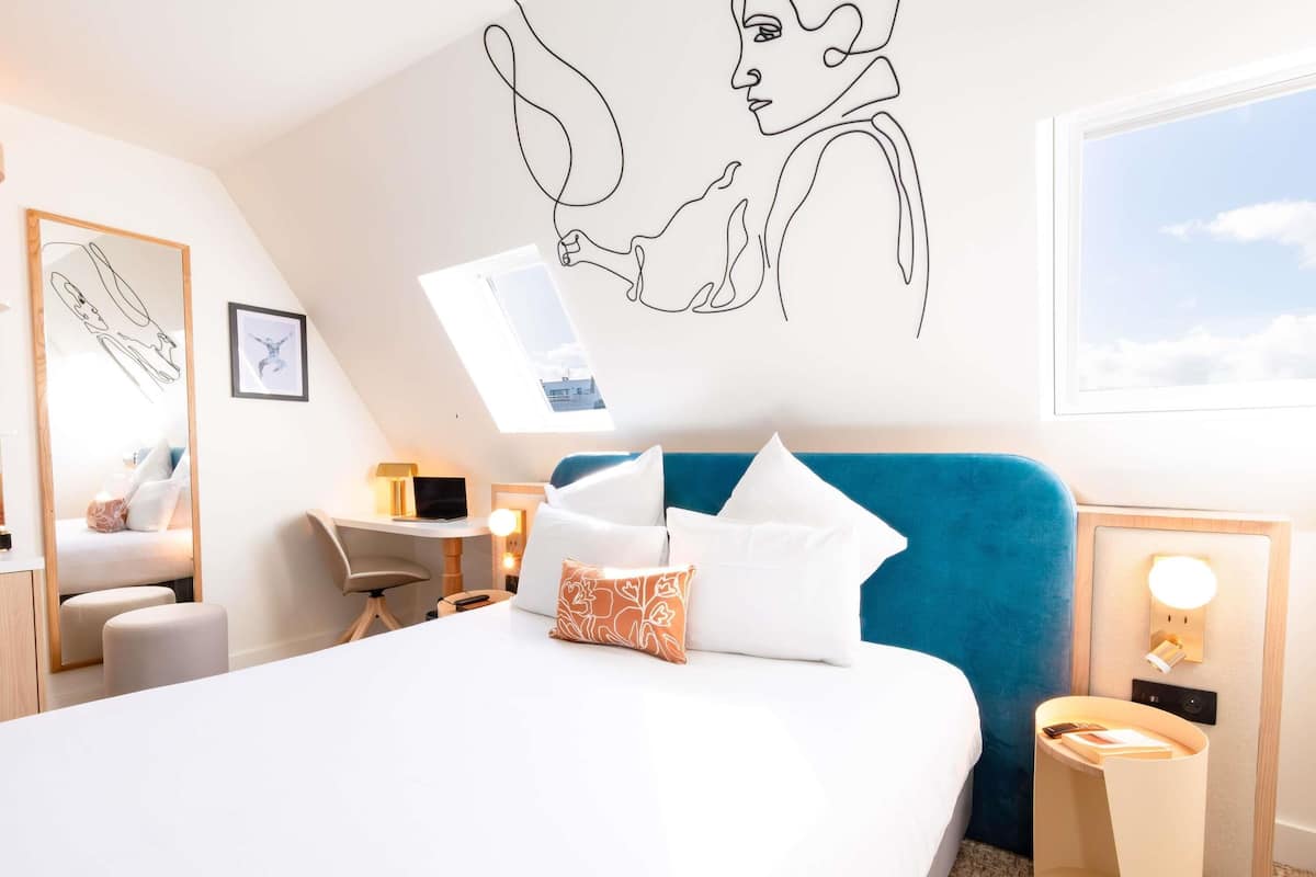 A modern hotel room with a large bed, a desk, a chair, and a skylight.