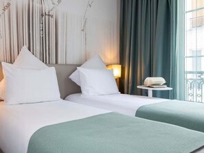 Hotellihuone, jossa on kaksi sänkyä, yöpöytä, lamppu ja näkymä kaupunkiin.