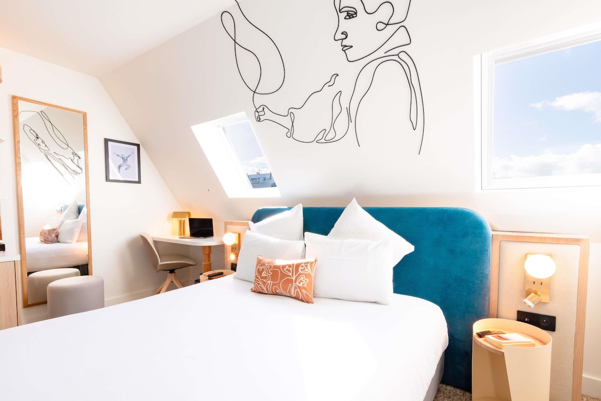 Une chambre d’hôtel moderne équipée d’un grand lit, d’un bureau, d’une chaise et d’une fenêtre de toit.