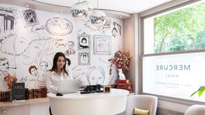 A woman at a reception desk with a laptop, surrounded by books and framed artwork on the wall. - Mercure Paris Montparnasse Raspail (Paris)