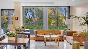 A spacious living area with a large window, a sofa, a coffee table, and a dining area with chairs and a table. - Hotel Roma Aurelia Antica (Rome)