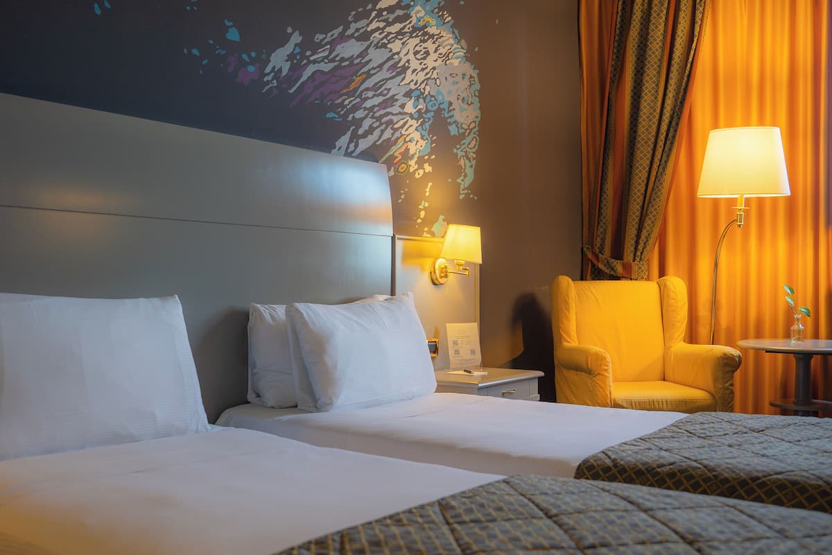 A hotel room with two beds, a large headboard, a chair, a table, and a wall mural.