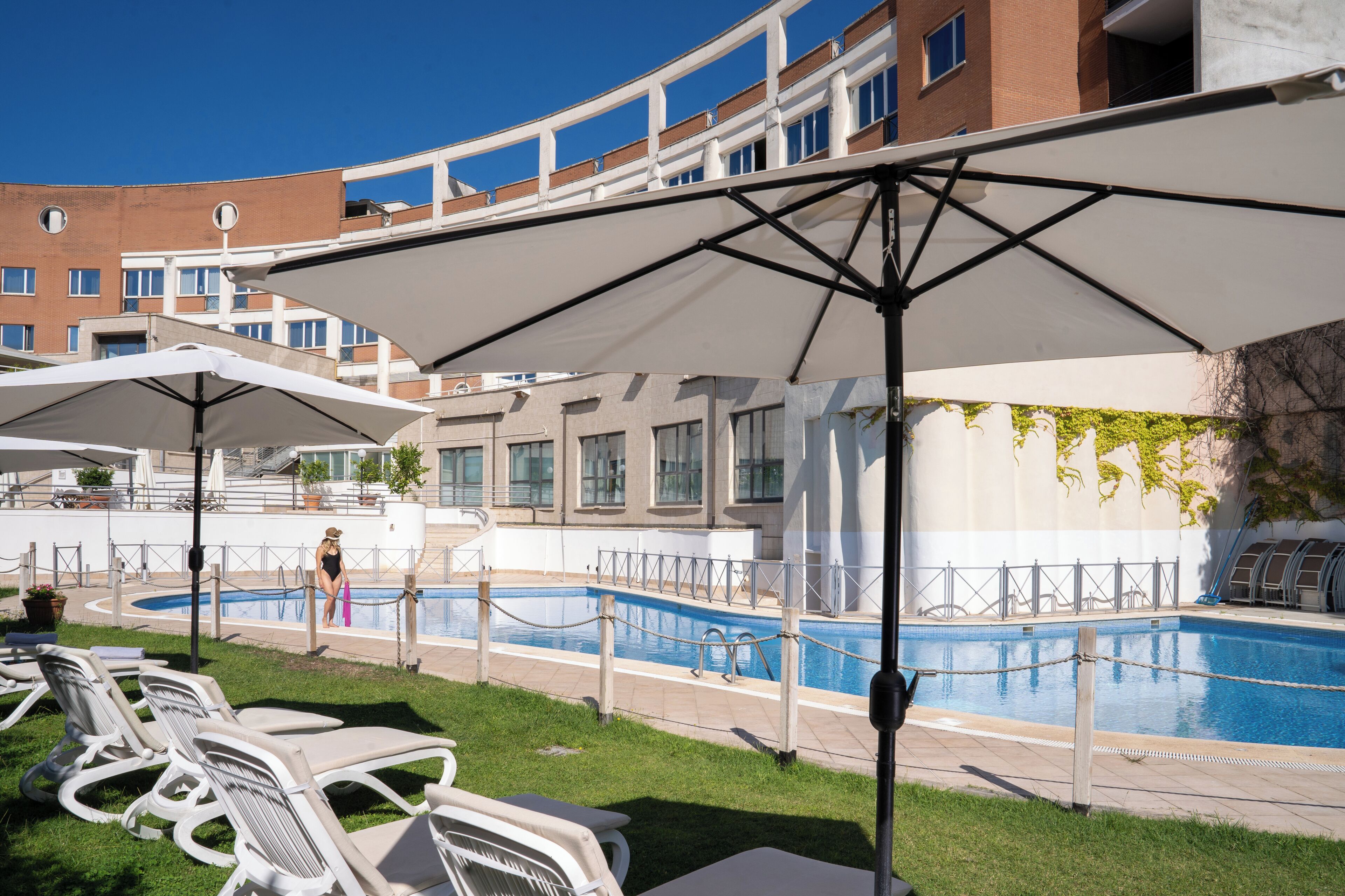A pool area with lounge chairs and umbrellas, surrounded by a building with multiple windows and a brick facade.