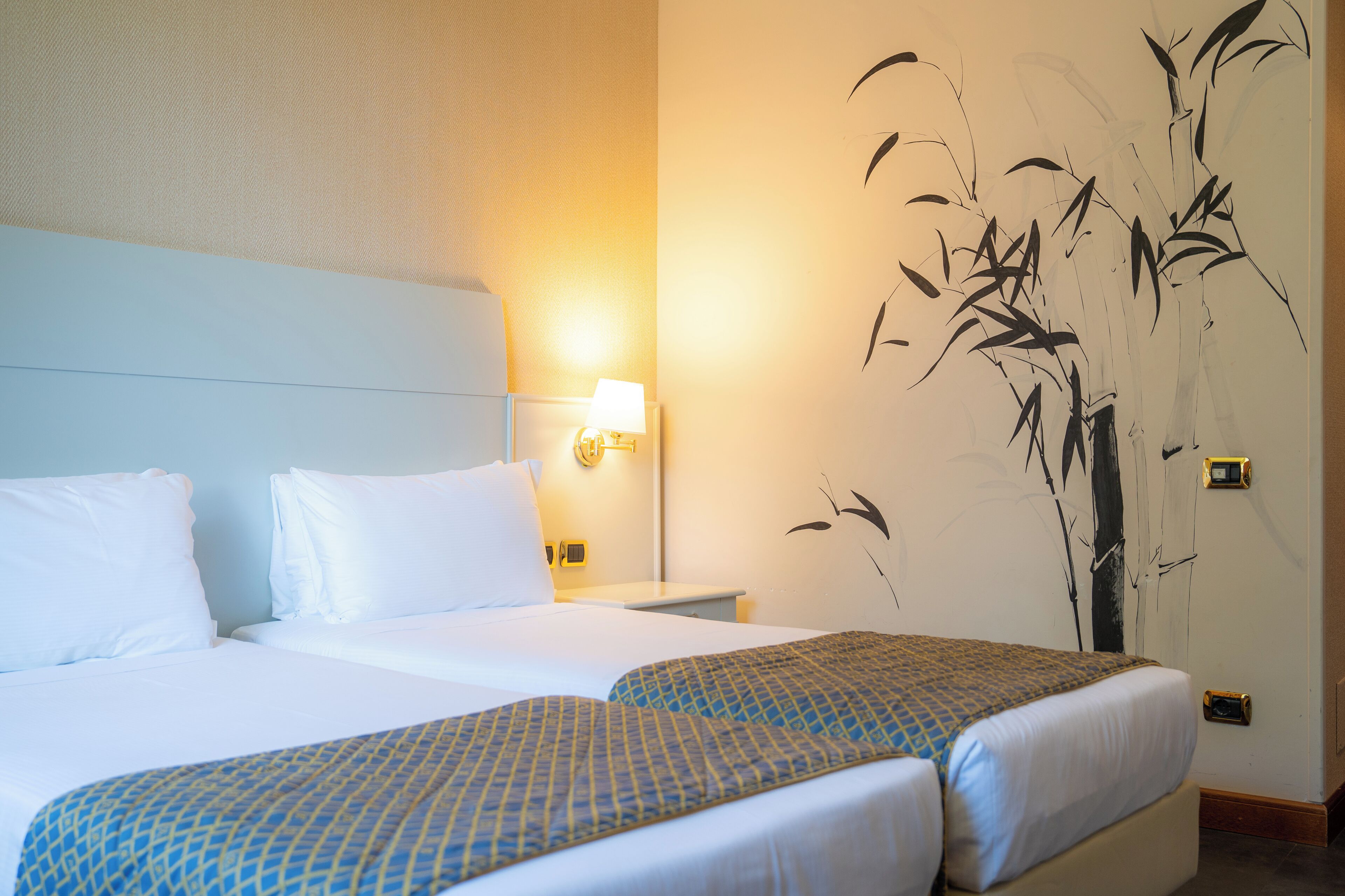 Habitación de hotel con dos camas, una mesita de noche, una lámpara de pared y un mural grande.
