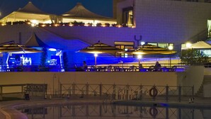 A pool area with a reflection of a building and a bar area with umbrellas. - Hotel Roma Aurelia Antica (Rome)