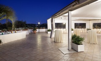 An outdoor patio area with white tables and chairs, potted plants, and a tiled floor.