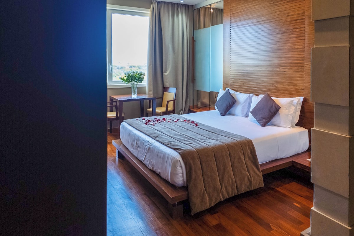 A modern hotel room with a wooden bed, a desk, and a chair.