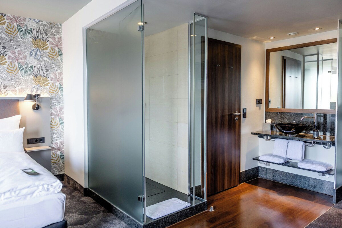 A modern bathroom with a glass shower enclosure, a wooden door, a large mirror, and a sink with a towel rack.