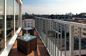 A balcony with wicker furniture and glass tables, overlooking a cityscape with buildings. - Flemings Hotel Frankfurt Main-Riverside (Frankfurt)