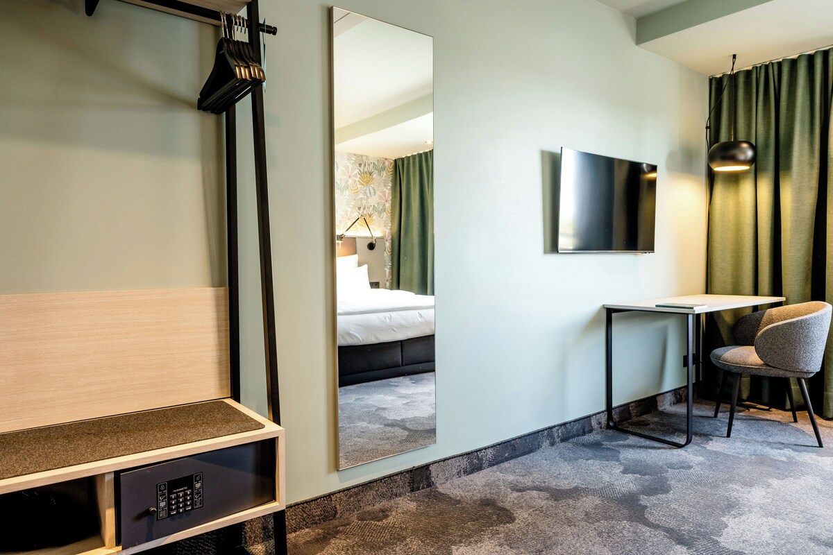 A hotel room with a bed, a desk, a chair, a TV, and a mirror.
