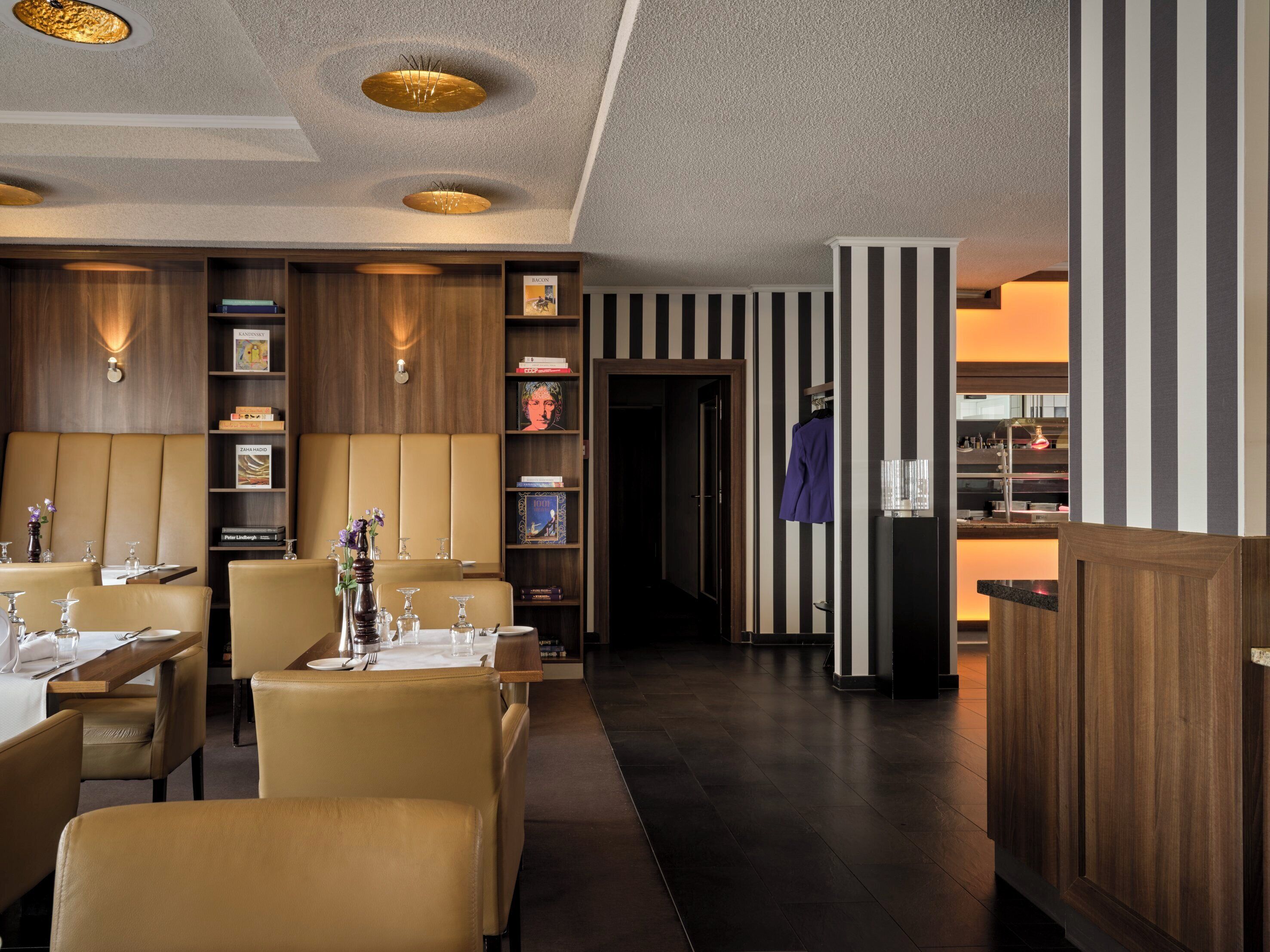 Un restaurante con una decoración moderna, que presenta paredes a rayas, paneles de madera y una zona central de comedor con mesas y sillas.