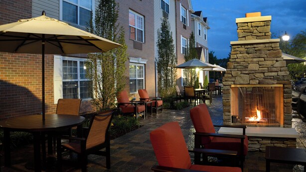 An outdoor patio area with stone fire pit, outdoor seating, and umbrellas. - Towneplace Suites by Marriott East Lansing (East Lansing)