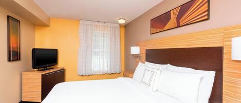 A hotel room with a large bed, a television on a wooden cabinet, a window with curtains, and a wall-mounted picture.