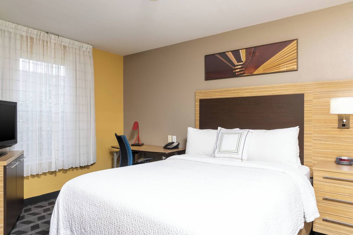 A hotel room with a large bed, a desk with a telephone, a television, and a wall-mounted artwork.