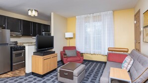 A compact living space with a kitchenette, a television, a sofa, and a red armchair. - Towneplace Suites by Marriott East Lansing (East Lansing)