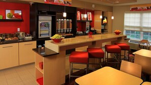 A modern restaurant with a bar area, red cushioned stools, and a variety of food and drink dispensers. - Towneplace Suites by Marriott East Lansing (East Lansing)