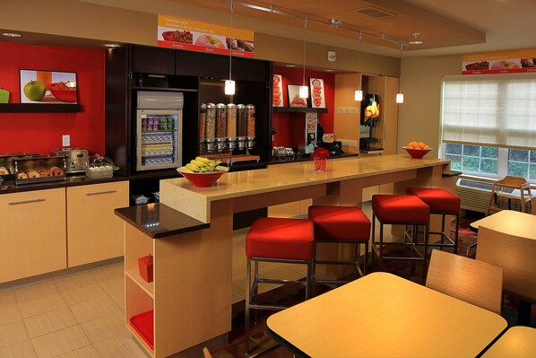 Un restaurante moderno con una zona de bar, taburetes acolchados rojos y diferentes dispensadores de comida y bebidas.