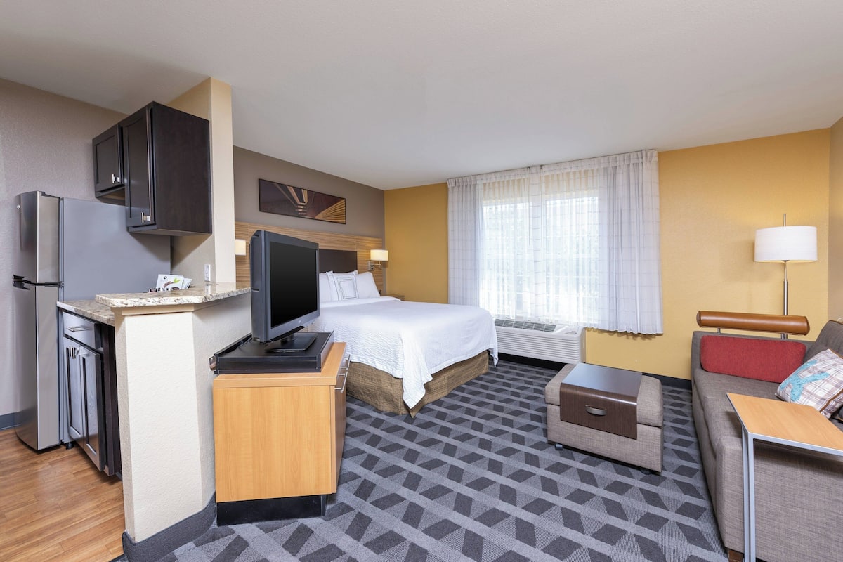 A hotel room with a bed, a desk, a sofa, a TV, and a minibar.