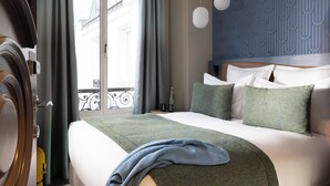 A hotel room with a bed, curtains, a window, and a wall with a textured pattern. - Hôtel L'Ormaie & Spa (Paris)