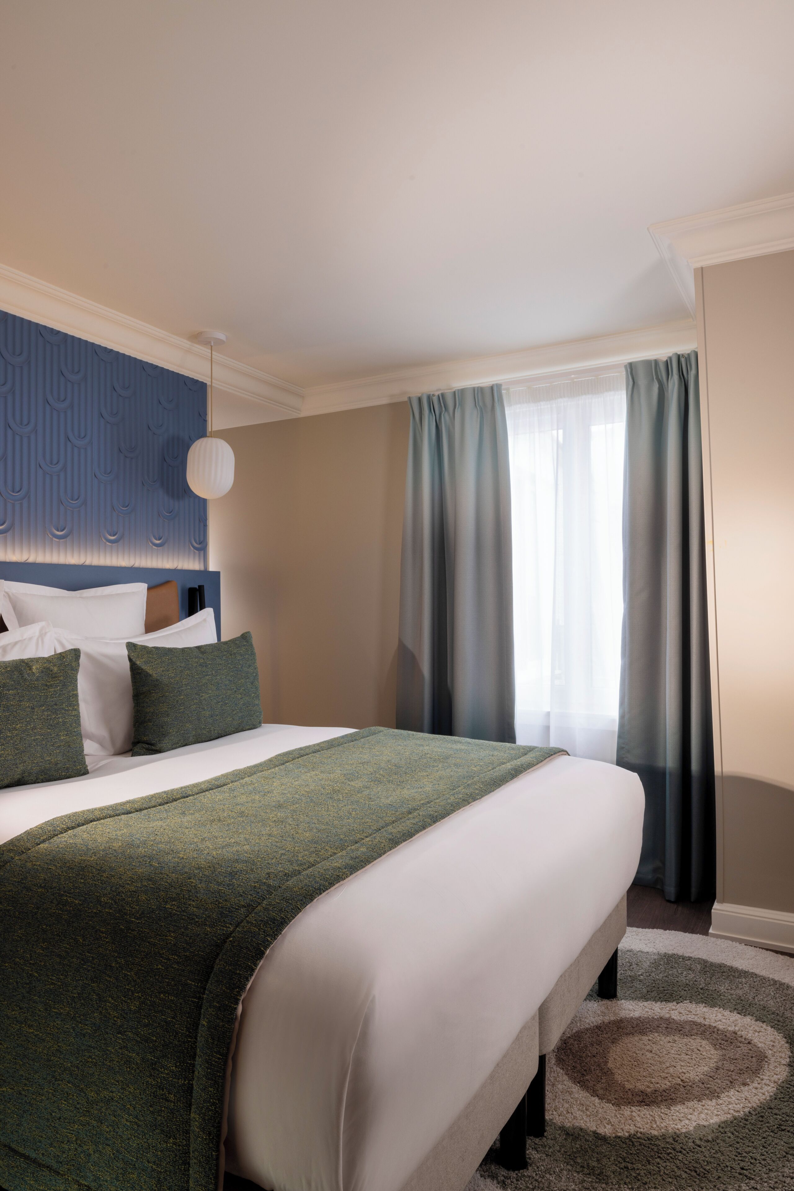 Een hotelkamer met een groot bed, een blauw hoofdeinde, een raam met gordijnen en een vloerbedekking.