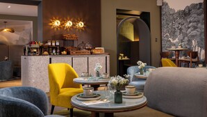 A modern hotel room with a dining area, a sofa, a yellow armchair, and a large painting on the wall. - Hôtel L'Ormaie & Spa (Paris)