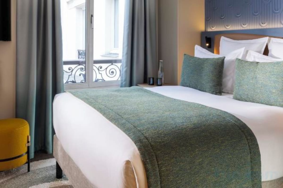 Habitación de hotel con cama, mesita de noche, ventana con cortinas y vista al exterior.