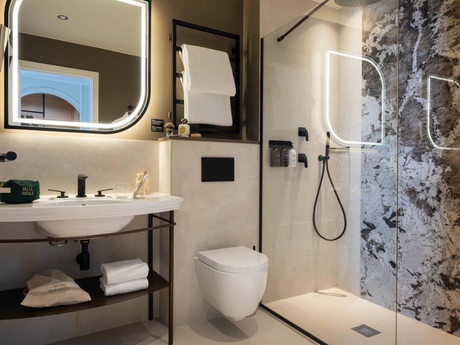 Un baño moderno con ducha de vidrio, lavamanos blanco y un espejo grande con iluminación integrada.