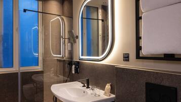Un baño moderno con ducha de vidrio, lavamanos blanco y espejo con marco iluminado.