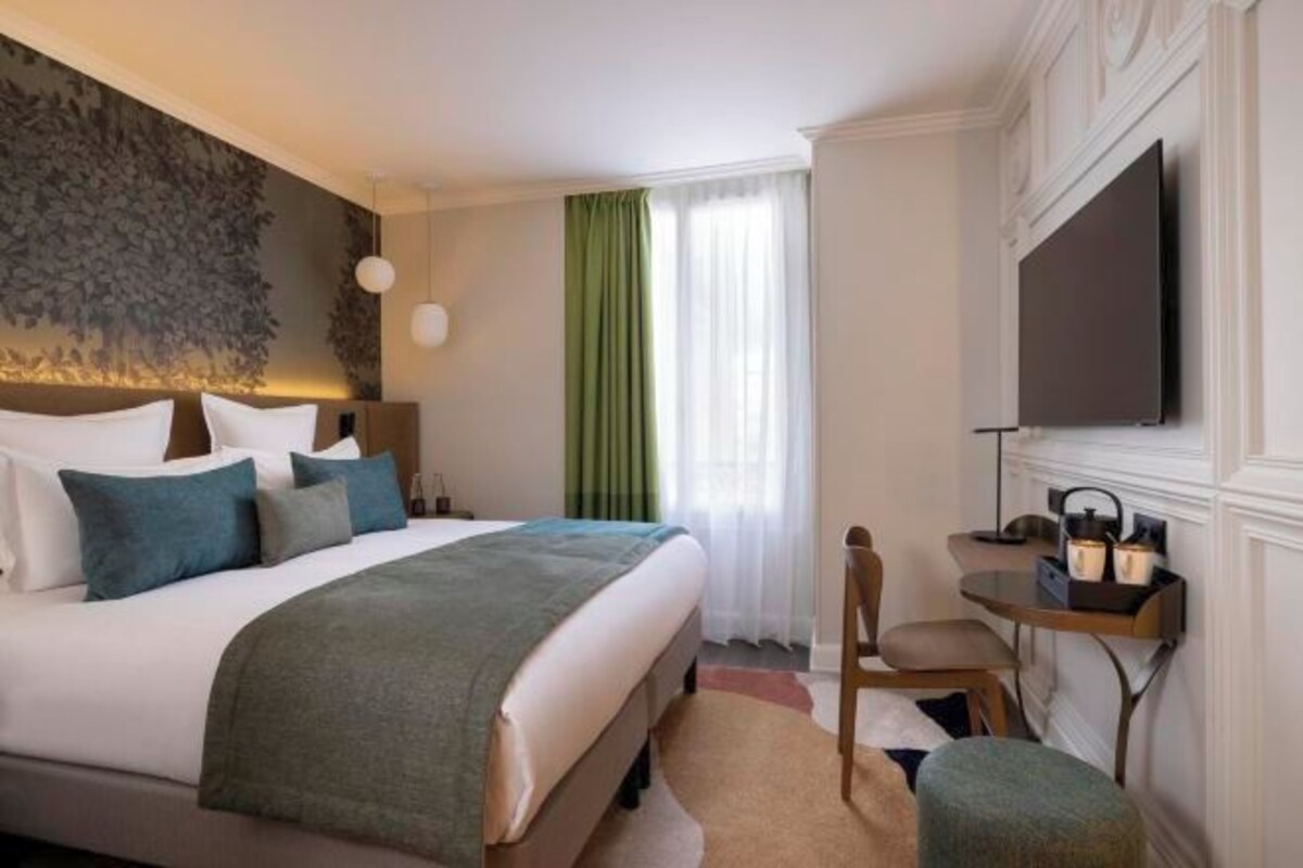 Habitación de hotel con cama, escritorio con silla, televisor y ventana grande con cortinas.