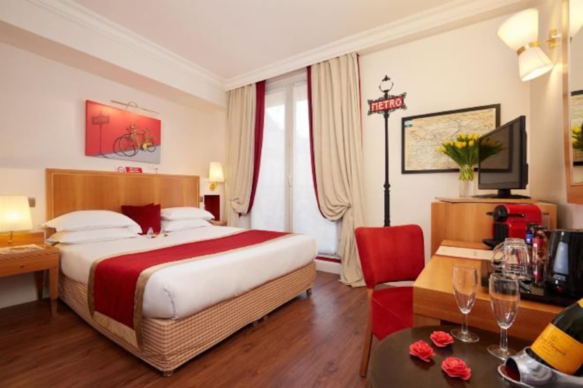 A hotel room with a bed, a desk, a chair, a television, and a minibar.