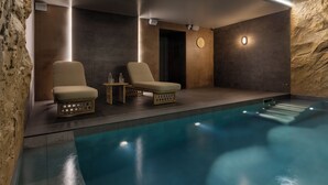 A modern indoor pool area with two lounge chairs, a small table, and a wall clock. - Hôtel L'Ormaie & Spa (Paris)