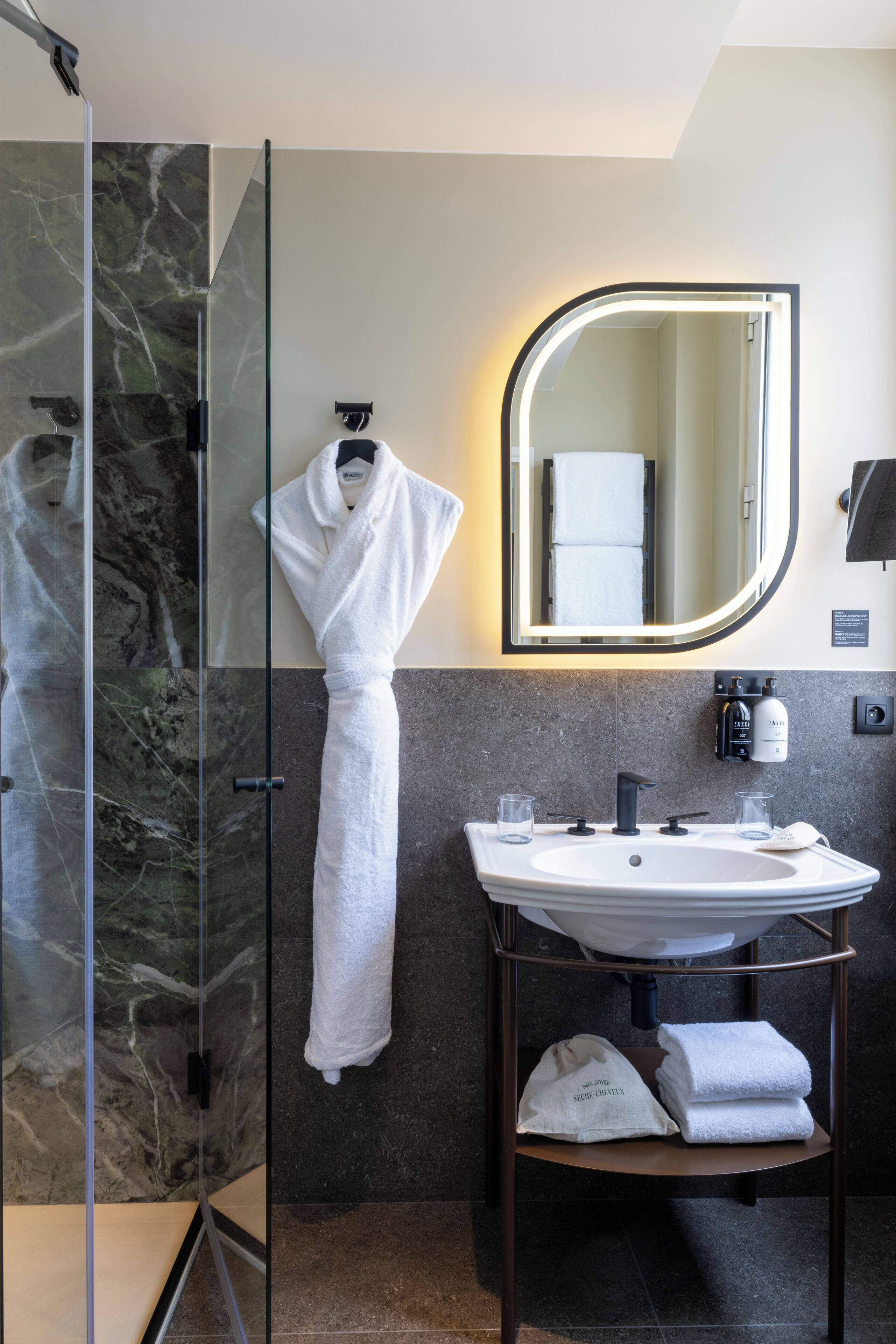 A modern bathroom with a glass shower, a white sink, and a mirror with a lighted frame.