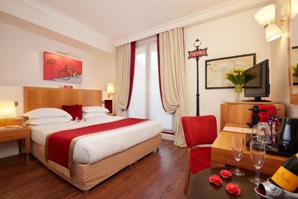 Una habitación de hotel con una cama, un escritorio con silla, un televisor y un minibar.